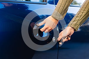Young woman unlocking her blue car door with key in hand.