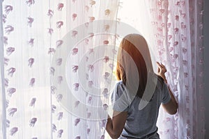 Young woman unveil curtain and looking out of window in the morning