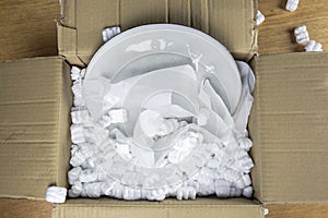 Young woman unwrapping delivery package,online shopping package. fragile cardboard box with plate at home top view, stylish