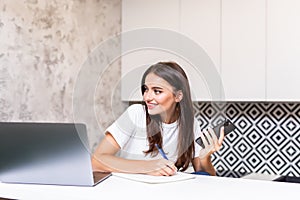 Young woman use mobile phone and writing notes while sitting at her desk. Pretty caucasian female working in home office