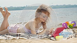 Young woman uses computer tablet on the beach, river bank