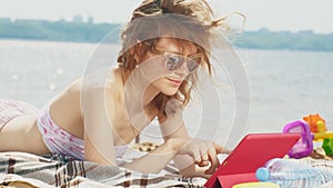 Young woman uses computer tablet on the beach, river bank