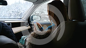 A young woman uses a mobile phone while sitting in the front passenger seat in a car.