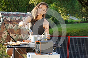 Young woman uses solar panel outdoors on camping to generate electricity for cooking