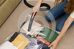 A young woman uses a vacuum cleaner to extract air from a transparent vacuum bag with warm things. Hermetic bag for saving space