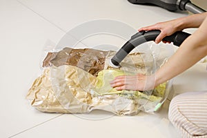 A young woman uses a vacuum cleaner to remove air from a transparent vacuum bag with folded clothes. Hermetic bag for saving space