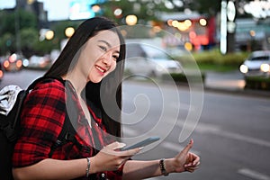 Young woman using application of taxi service app on smart phone in the city at night.