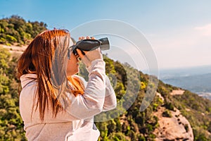 young woman using binoculars to spot birds in the sky, while hiking on top of mountain. person observing the horizon.