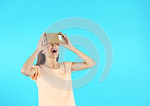 Young woman using cardboard virtual reality headset on color background.