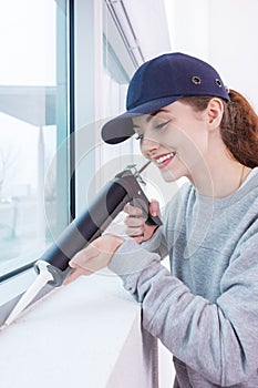 Young woman using caulking gun on window frame