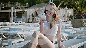 Young woman using cellphone while lying on sunbed on beach