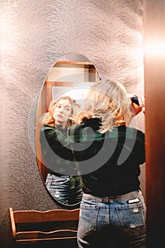 Young woman using curling iron looking at herself in the mirror