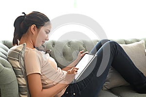 Young woman using digital tablet surfing internet, read news and distance online study on a couch.