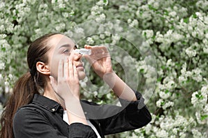 Young woman using eye drops near blooming tree. Allergy concept