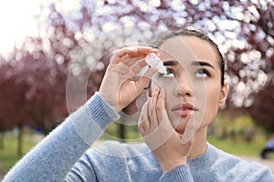 Young woman using eye drops near blooming trees. Allergy concept