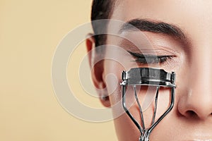 Young woman using eyelash curler on beige background, closeup. Space for text