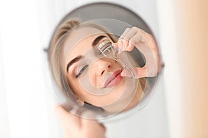 Young woman using eyelash curler in front of mirror at home