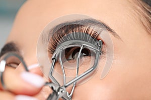 Young woman using eyelash curler on grey background, closeup