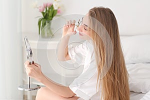 Young woman using eyelash curler at home