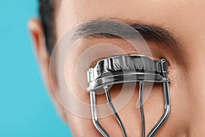 Young woman using eyelash curler on light blue background, closeup