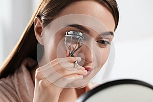 Young woman using eyelash curler near mirror, closeup
