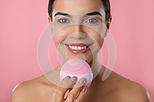 Young woman using facial cleansing brush on background, closeup. Washing accessory
