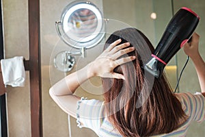 Young woman using hair dryer near mirror at home or hotel. Hairstyles and lifestyle concepts