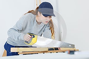 Young woman using hand saw in woodshop photo