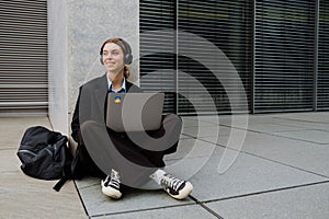 Young woman using headphones and laptop while sitting outdoors