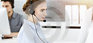 Young woman using headset and computer while talking with customers online. Group of Call center operators at workin