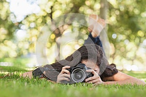 Young woman using her camera for taking a picture lying on a lawn