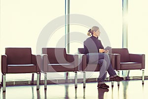 Young woman using her digital tablet pc at an airport lounge, modern waiting room, with backlight