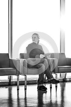 Young woman using his digital tablet pc at an airport lounge, modern waiting room, with backlight