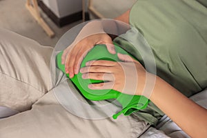 Young woman using hot water bottle to relieve cystitis pain on bed indoors, closeup