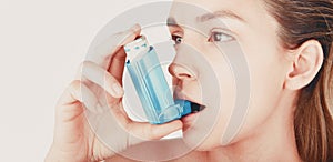 Young woman using inhaler during asthmatic attack at home, closeup, white background photo