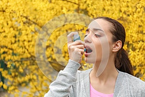 Young woman using inhaler near blooming tree. Allergy concept