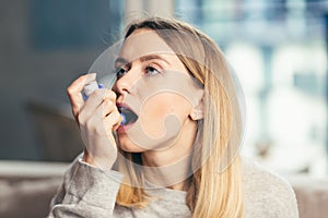 Young woman using inhaler while suffering from asthma at home
