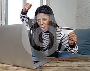 Young woman using laptop angry and stressed about her credit card bill