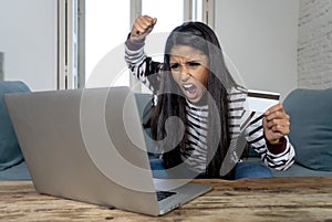 Young woman using laptop angry and stressed about her credit card bill