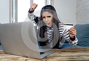 Young woman using laptop angry and stressed about her credit card bill