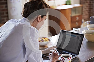 Young woman using laptop at breakfast, over shoulder view