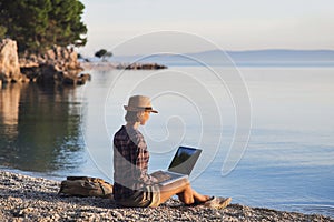 Young woman using laptop computer on a beach. Freelance work concept