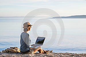 Young woman using laptop computer on a beach. Freelancer working by the sea, vacations, business, people,