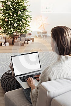 Young woman using laptop computer with blank empty mockup screen during Christmas holidays at home