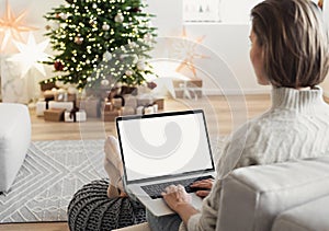 Young woman using laptop computer with blank empty mockup screen during Christmas holidays at home