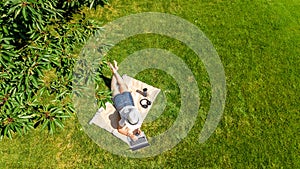 Young woman using laptop computer in park, student girl freelancer working and studying online outdoors sitting on grass