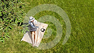 Young woman using laptop computer in park, student girl sitting on grass with headphones and laptop, aerial drone view