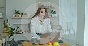 Young woman using laptop computer. Portrait of business woman watching news at laptop screen and drinking coffee at home