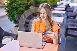 Young woman using laptop and credit card sitting on table at coffee shop terrace