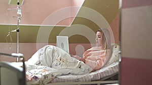 Young woman using laptop having video chat on hospital bed